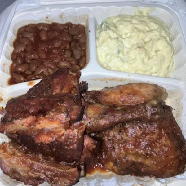 A takeout container with BBQ ribs, chicken, baked beans, and potato salad.