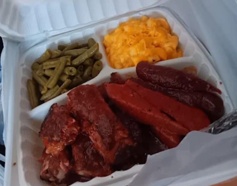 Barbecue ribs, hot dogs, green beans, and macaroni and cheese in a takeout container.