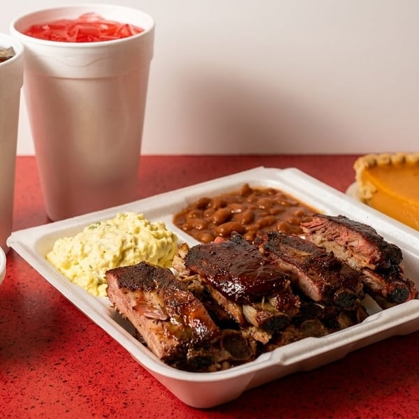 A takeout meal with BBQ ribs, baked beans, potato salad, green beans, two drinks, and pumpkin pie.